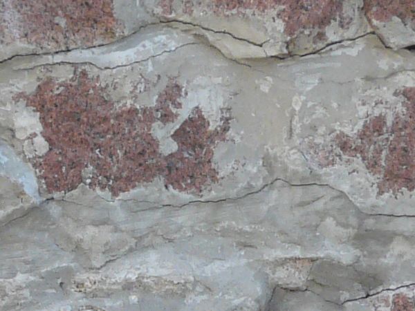Red stone set unevenly in concrete with cracks in between.